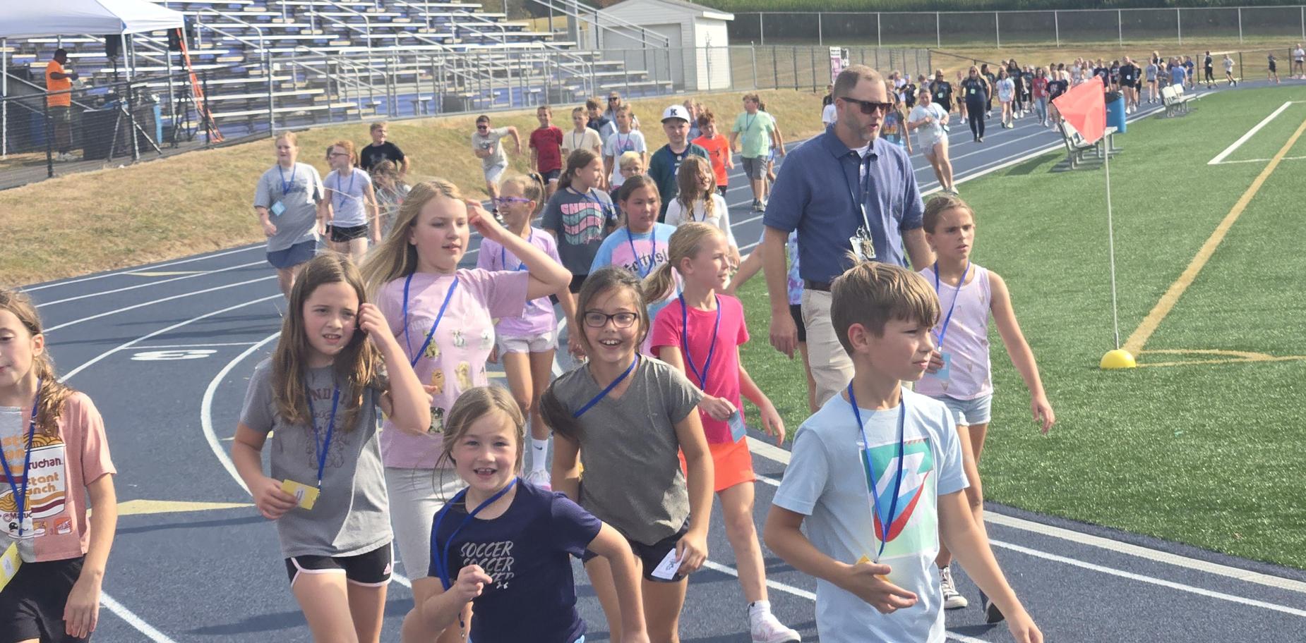 Students walking on a track, engaging in a school event with adults supervising.