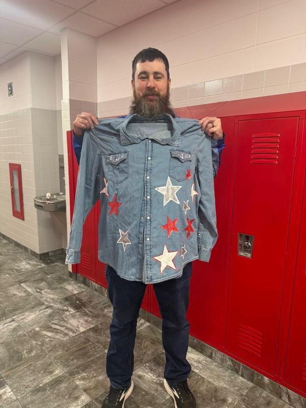 A man holding a star-patterned denim shirt while standing near red lockers.