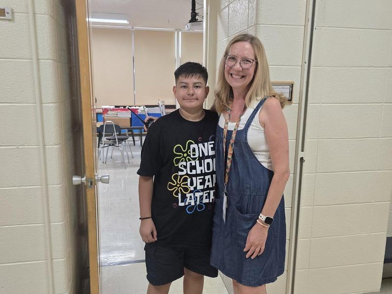 A boy and an adult woman smiling together in a school hallway.