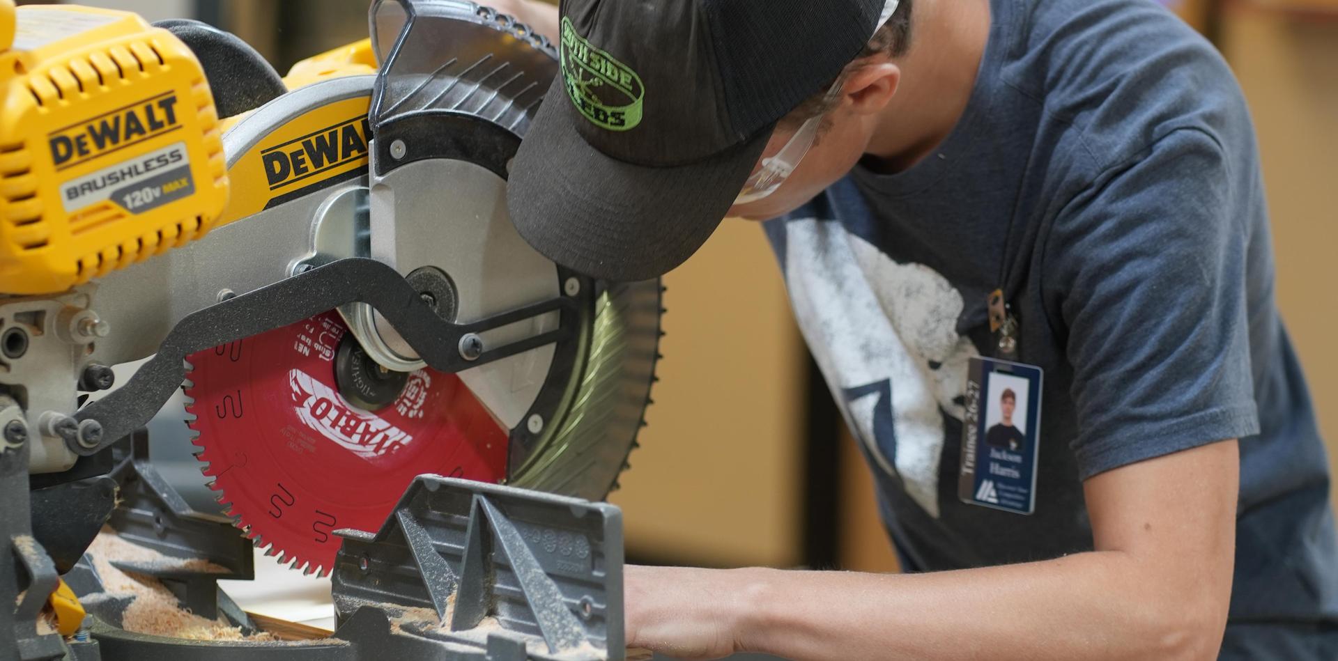 A person using a miter saw with a red blade in a workshop setting.