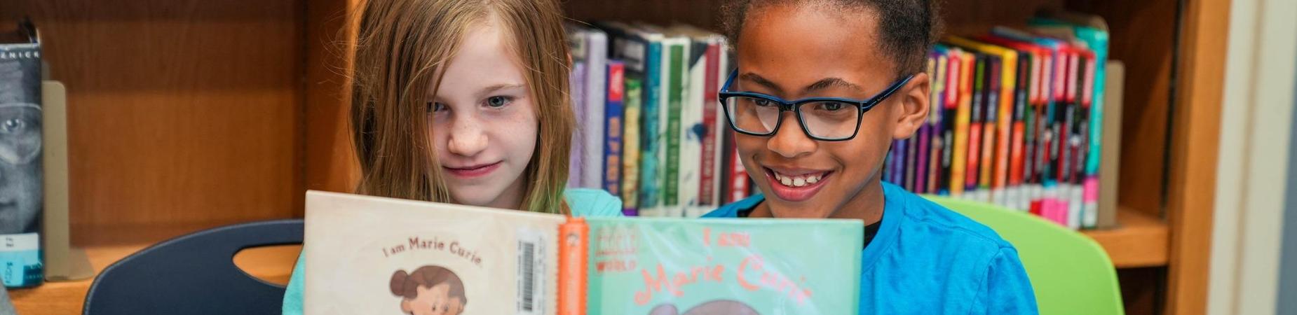 Two girls focused on their books in a library, creating a serene atmosphere filled with knowledge and imagination.