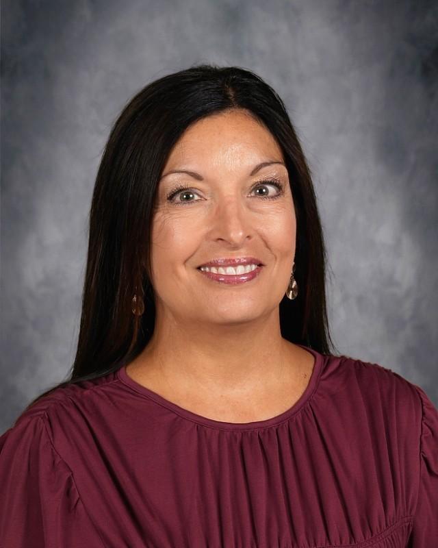 Smiling woman with long black hair, wearing a maroon blouse, in front of a neutral backdrop.