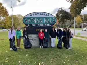 Students holding garbage bags in front of Nathan Hale High School sign.