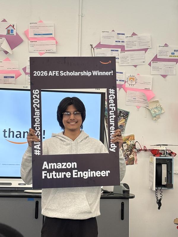 A student holds a scholarship frame, smiling in a classroom.