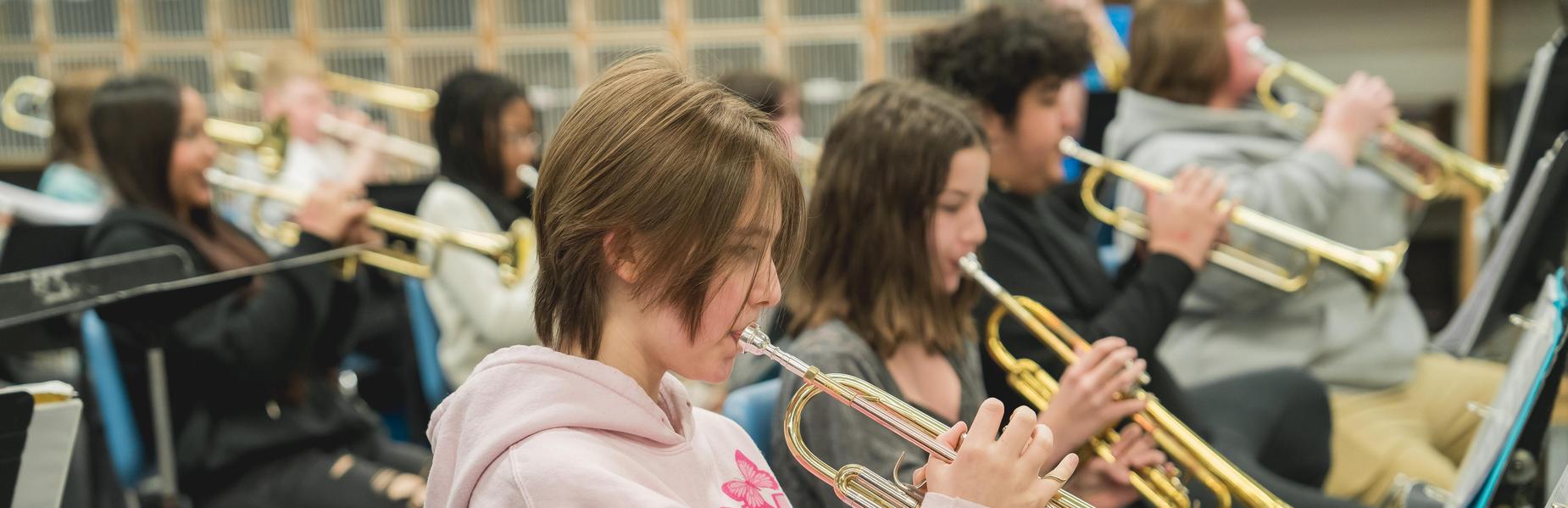 Band members play trumpets while seated in a music class.