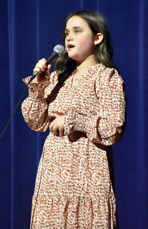 Girl in a patterned dress singing into a microphone on stage.