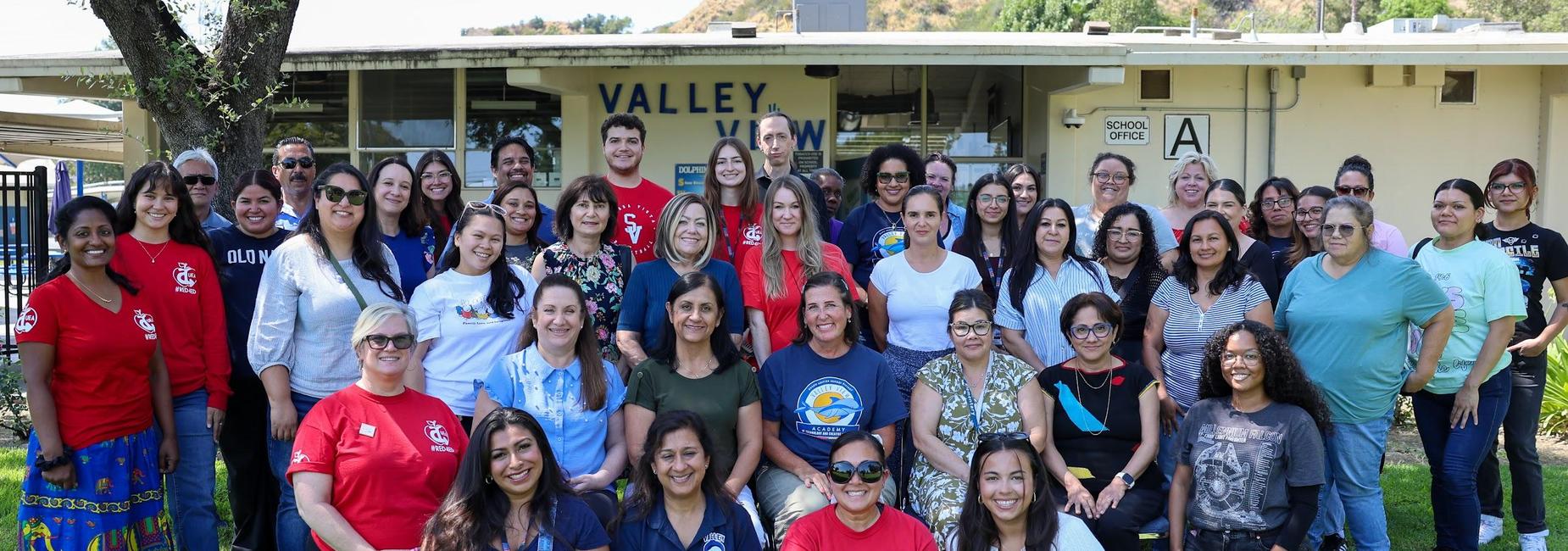Group photo of diverse people standing together outside a school building.