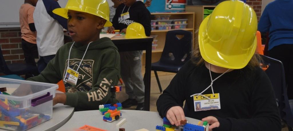 two students in hard hats construct with legos