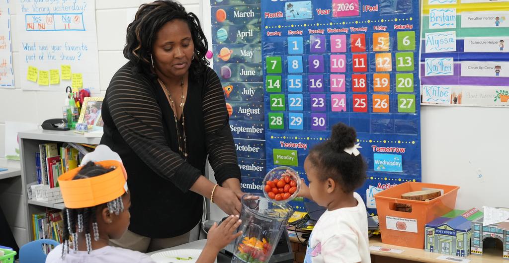 Students pour tomatoes into a container held by a teacher.