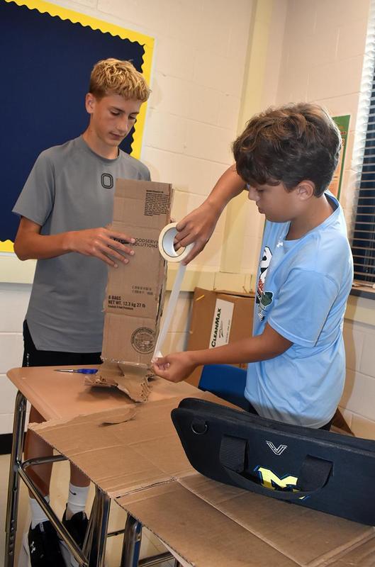 Two boys working with cardboard and tape at a desk.