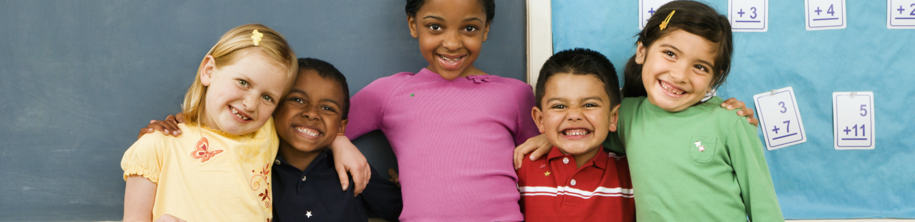 five children standing in front of a blackboard in a classroom