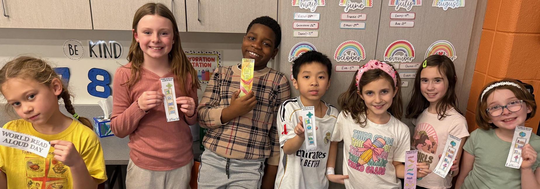 Seven children hold bookmarks and smile, celebrating World Read Aloud Day.