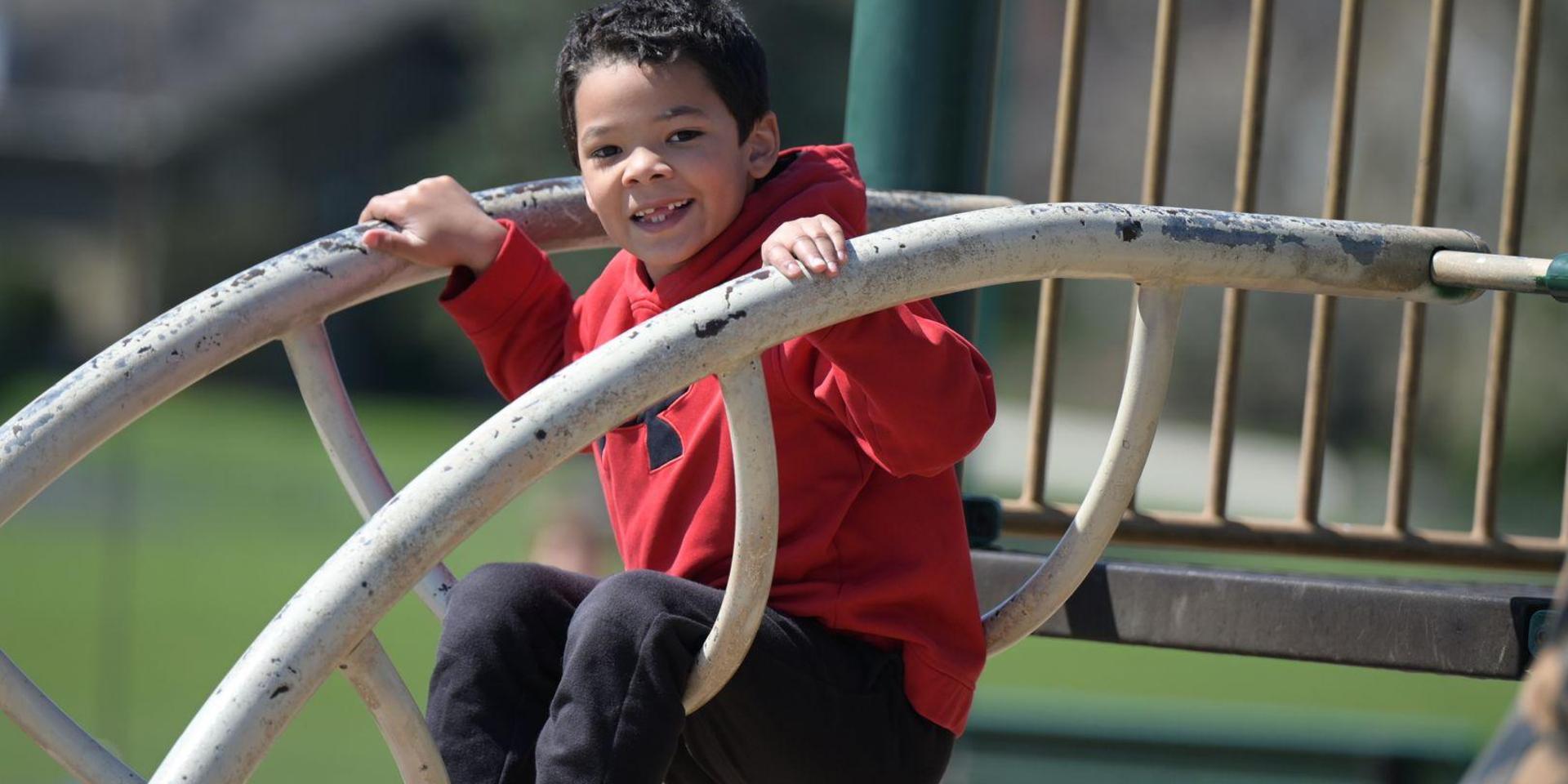 Child in a red hoodie happily playing on a playground structure.
