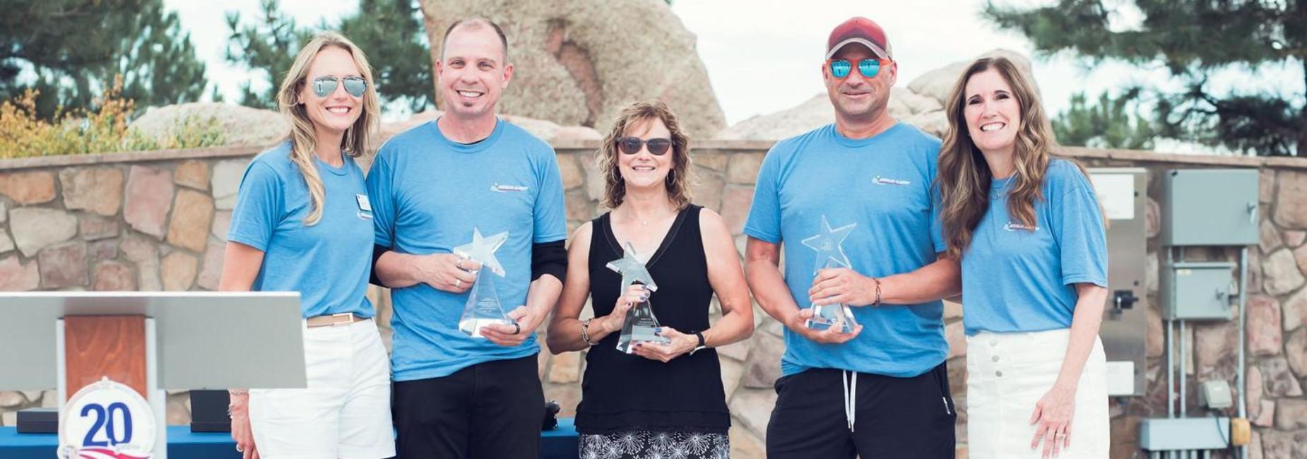 Group of five people holding awards at an outdoor event, smiling.