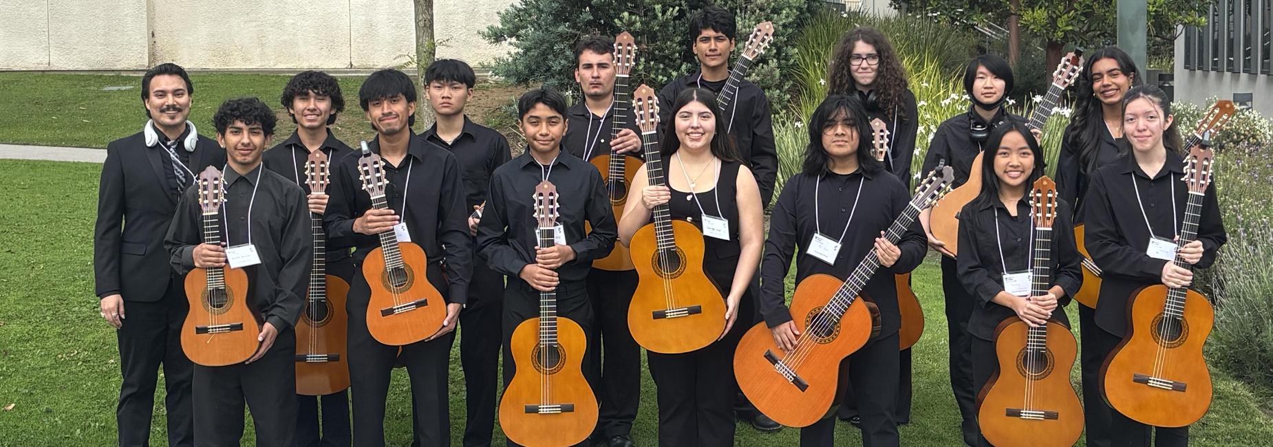 A group of musicians holding guitars outdoors, posing together in a grassy area.