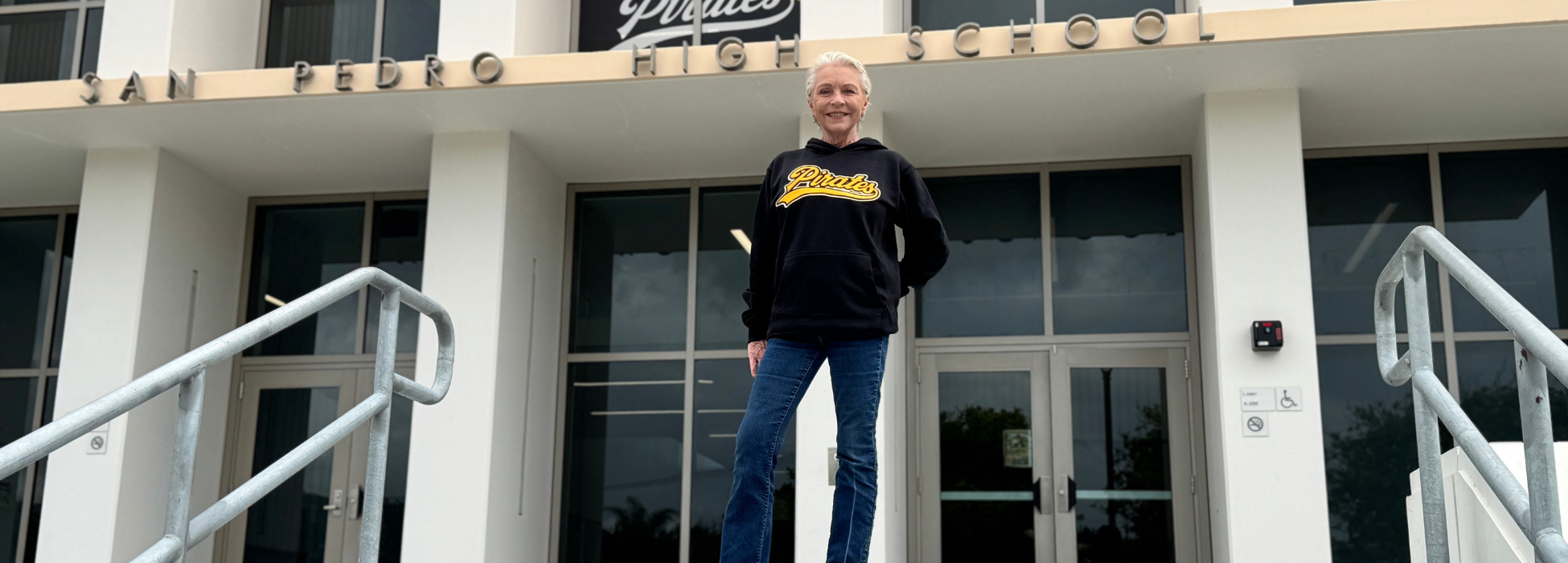 Woman in a hoodie standing on school steps in front of a high school building.