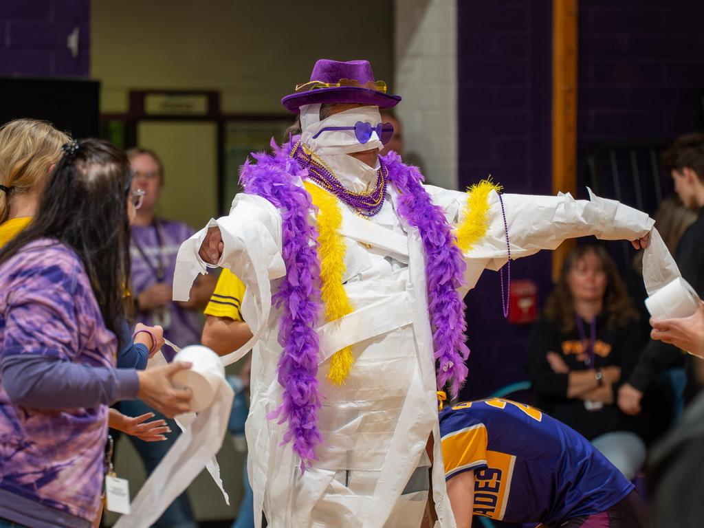 A faculty member completely wrapped in toilet paper and wearing a hat, glasses and feather boa.