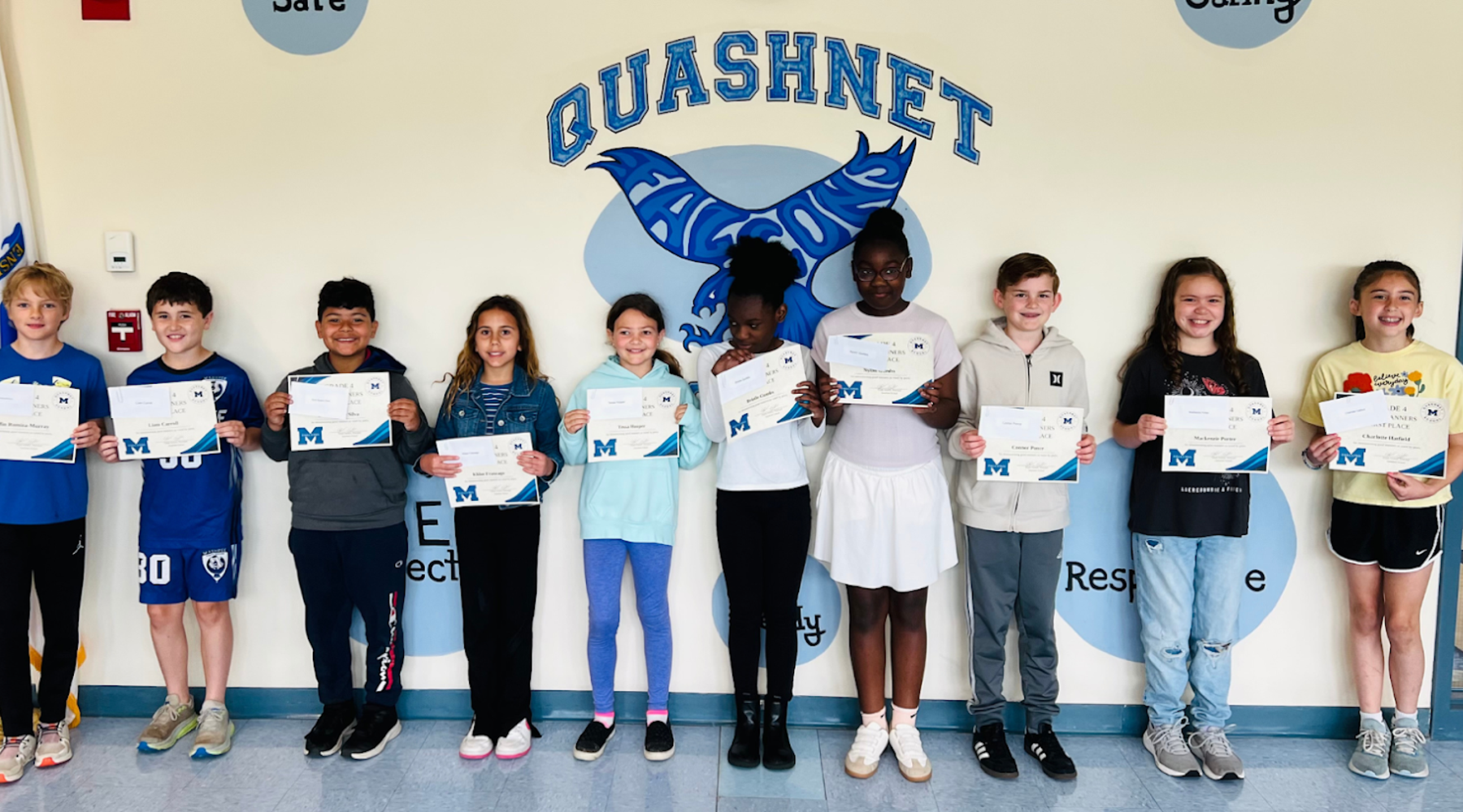 Students holding certificates in front of a wall with Quashnet logo.