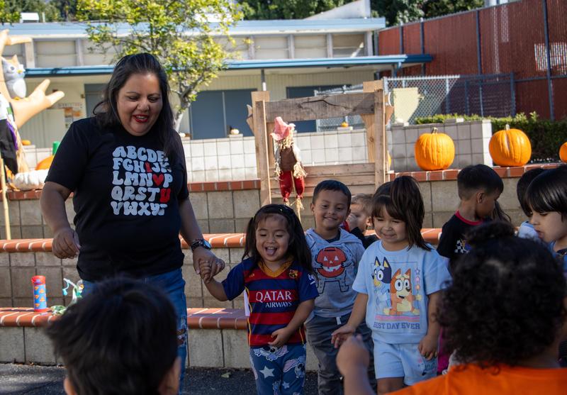 teacher smiles, holds hands with preschoolers.