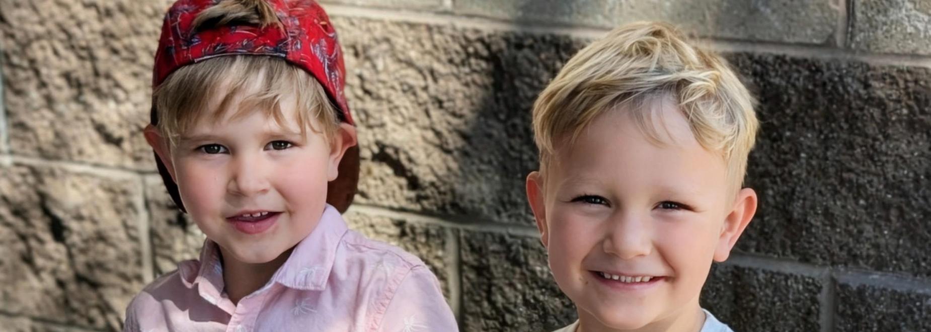 Two boys smiling, one in a pink shirt and the other in a graphic tee.