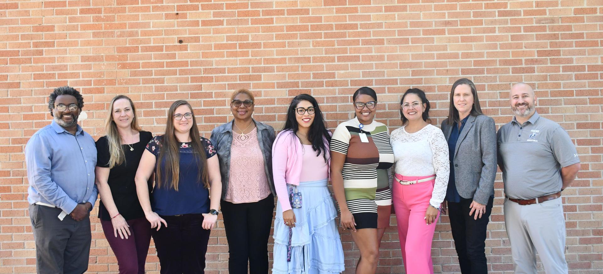 9 people standing behind the red/brown brick building.