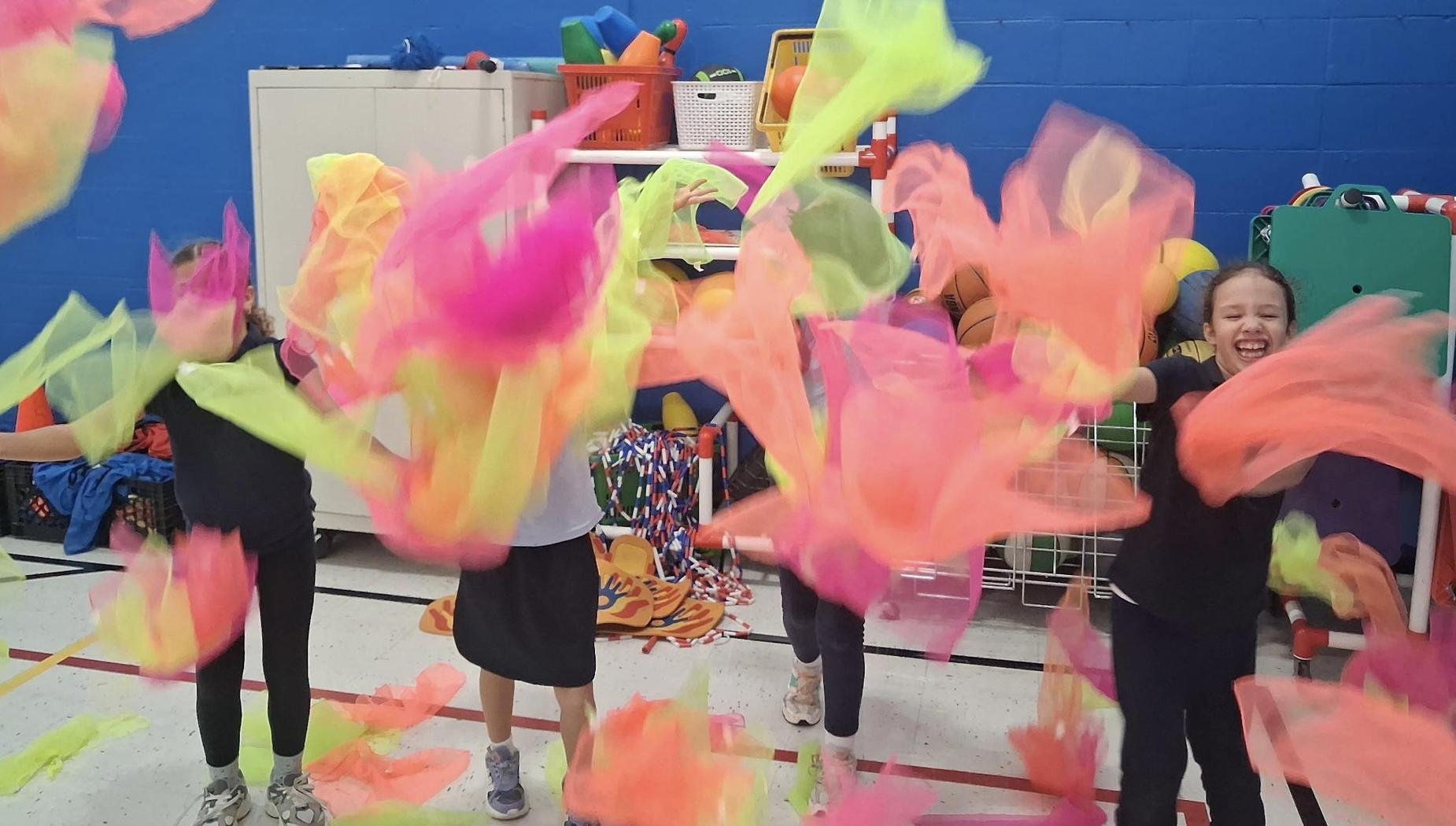 Kids joyfully waving bright colorful scarves in an indoor play area.