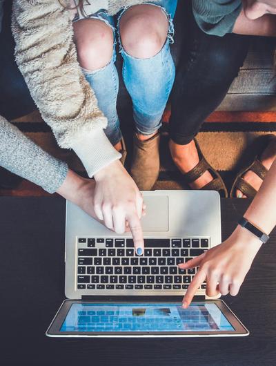 Three people pointing at a laptop screen, seated together on a couch.