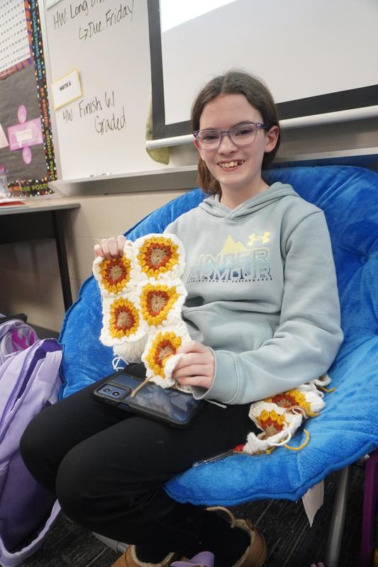 A student holds up several squares of sunflowers she will crochet together to make a tote bag.