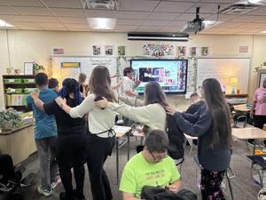 Students forming a line and dancing in a classroom filled with desks.