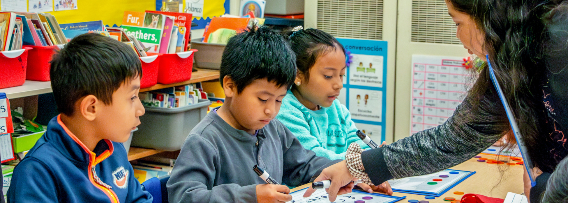 Three children engaged in a classroom activity with a teacher guiding them.
