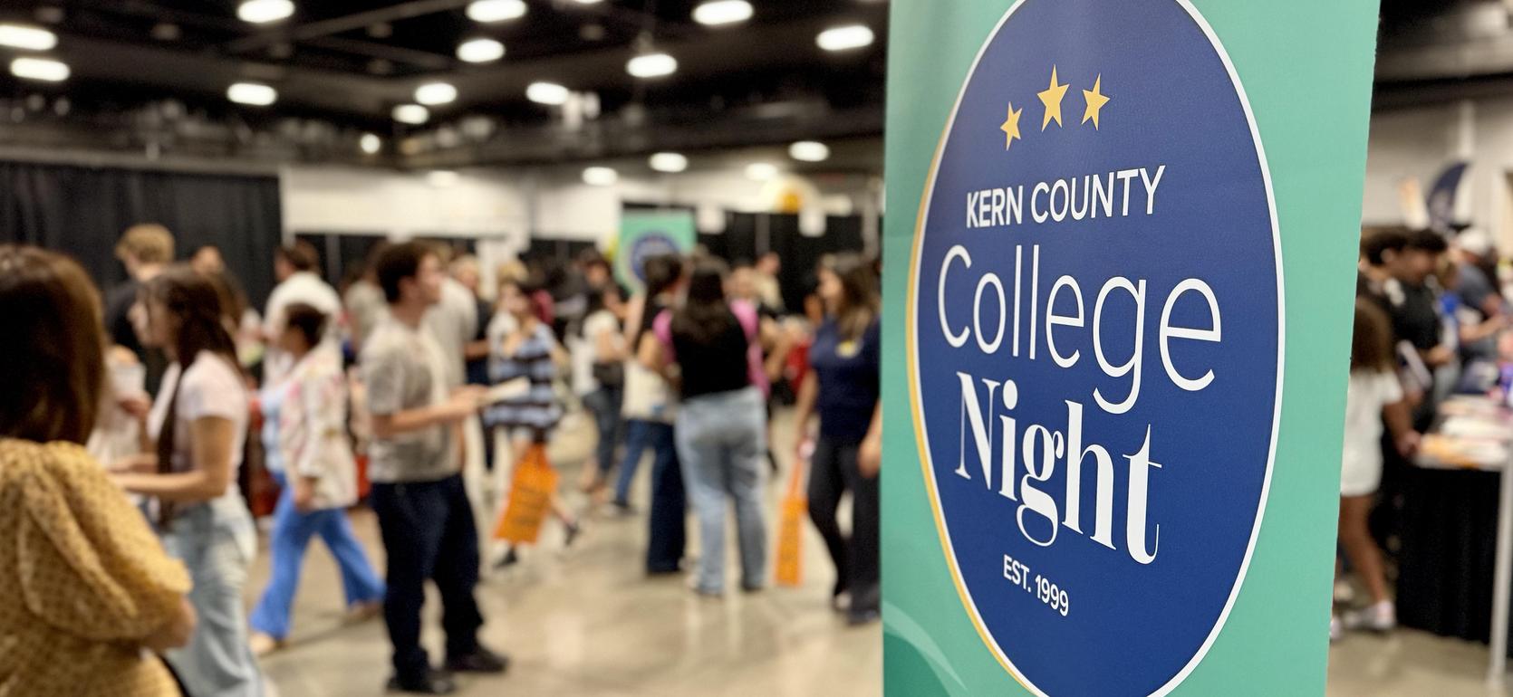 Kern County College Night sign with attendees in the background.