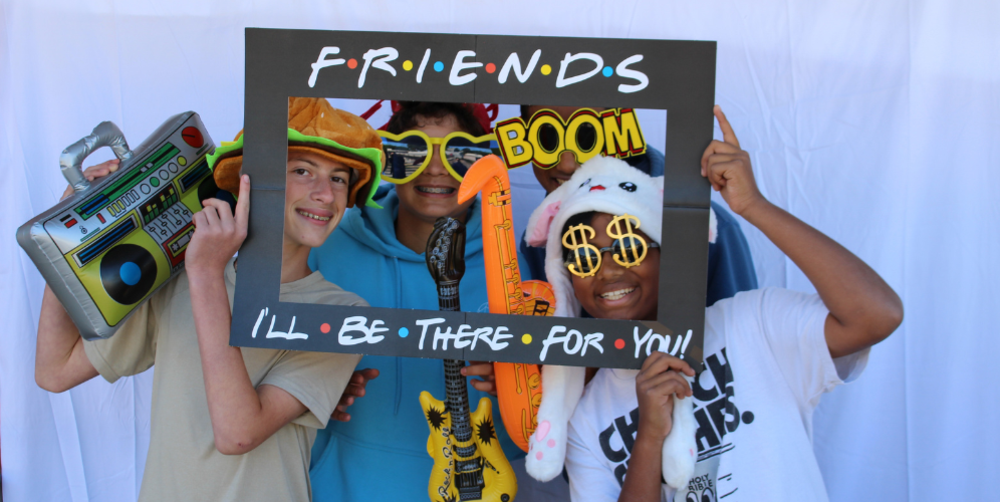 Three boys pose with fun props in a photo frame, celebrating friendship.