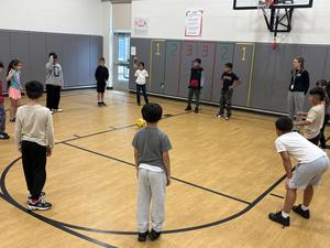 Students kick a soccer ball to each other in the gym.