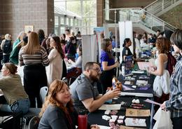 Crowd of people at tables engaging in a vibrant expo or fair setting.