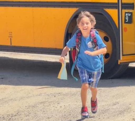 Picture of a student excitedly running onto campus from the school bus on the first day of school