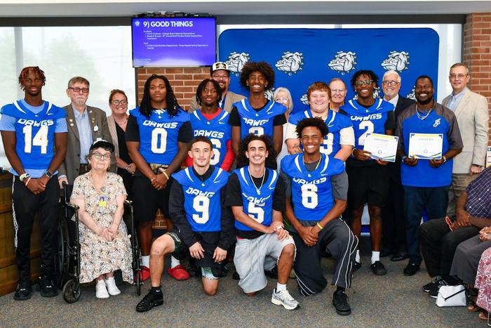 A group of football players, a coach, and school board members smiling and holding an award