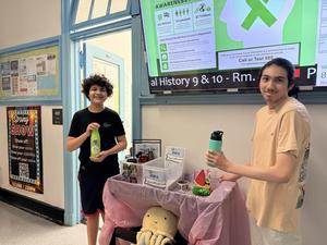 Two students holding water bottles in front of an information screen.