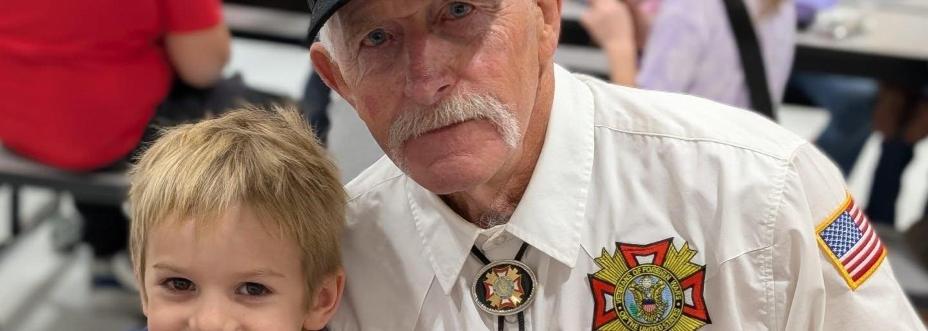 Elderly man in uniform cuddling a young boy, both smiling for the camera.