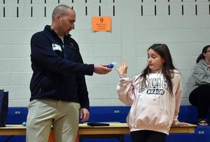 A man hands a blue object to a girl in a gym setting.