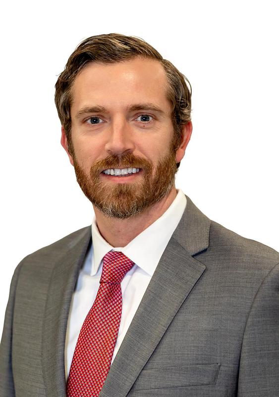 headshot man in suit jacket with red tie smiling