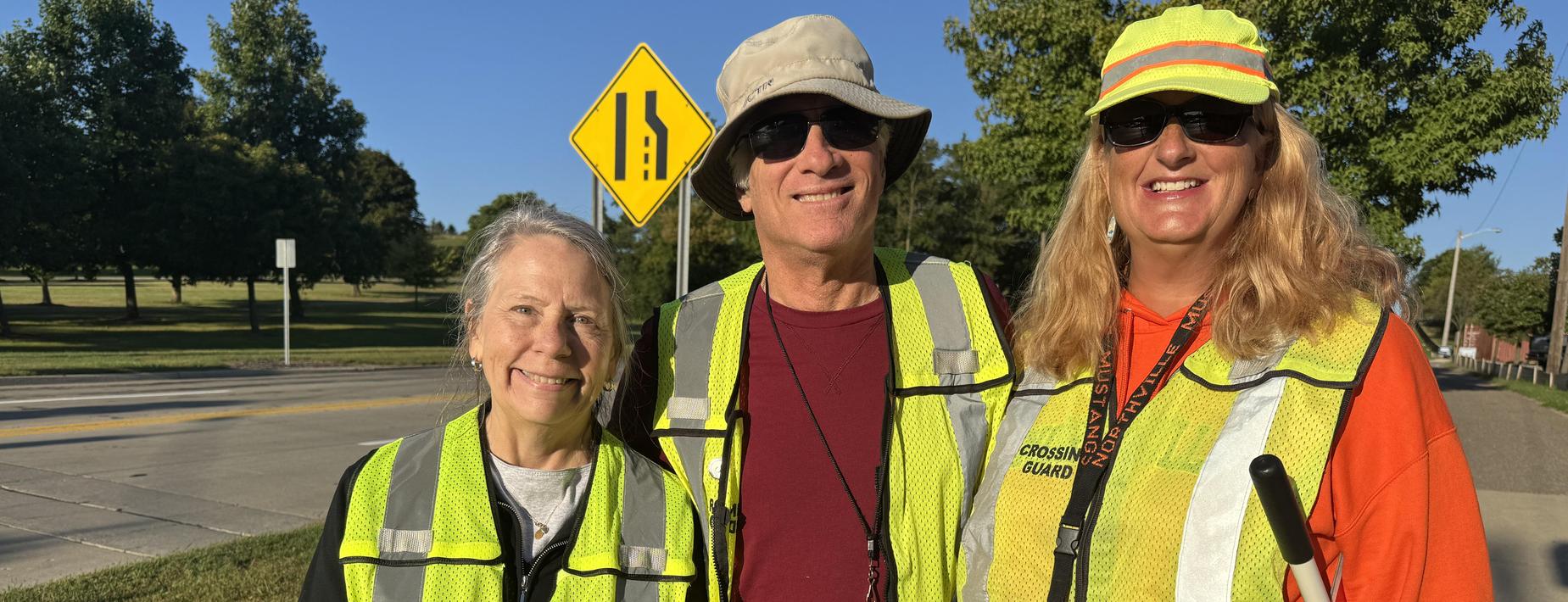 Three people standing together in bright safety vests.