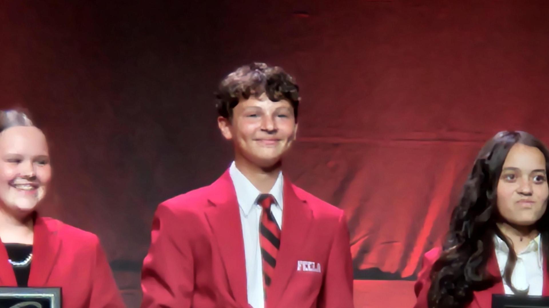 Three individuals in red blazers holding awards on a stage.