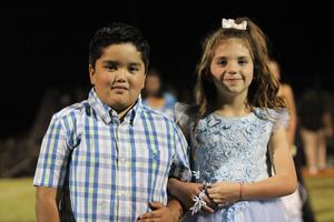 Two children, a boy in a plaid shirt and a girl in a blue dress, pose together.