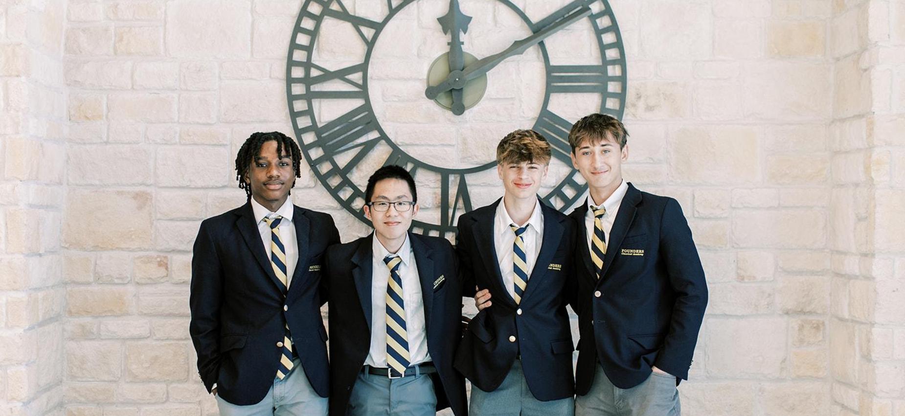 Four high school students in navy blazers stand beneath a large clock
