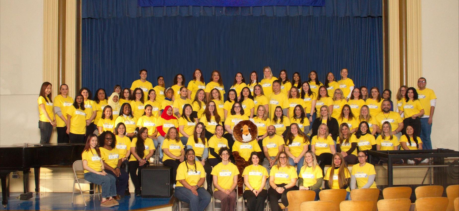 Group of people wearing yellow shirts posing together on a stage.