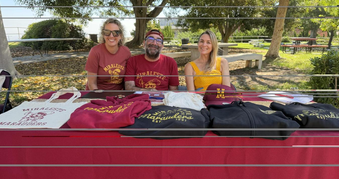 Three people pose behind a table covered with school merchandise.