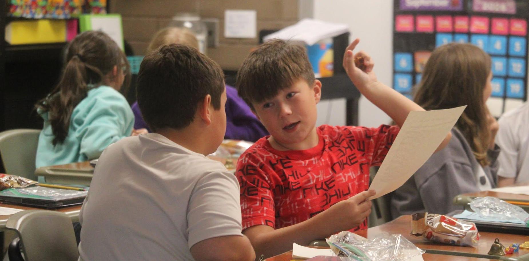 Two children engaged in conversation at a classroom table.