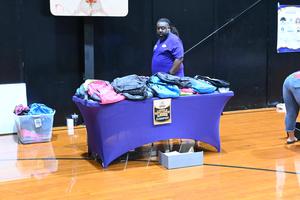 Table displaying backpacks and a person wearing a purple shirt.