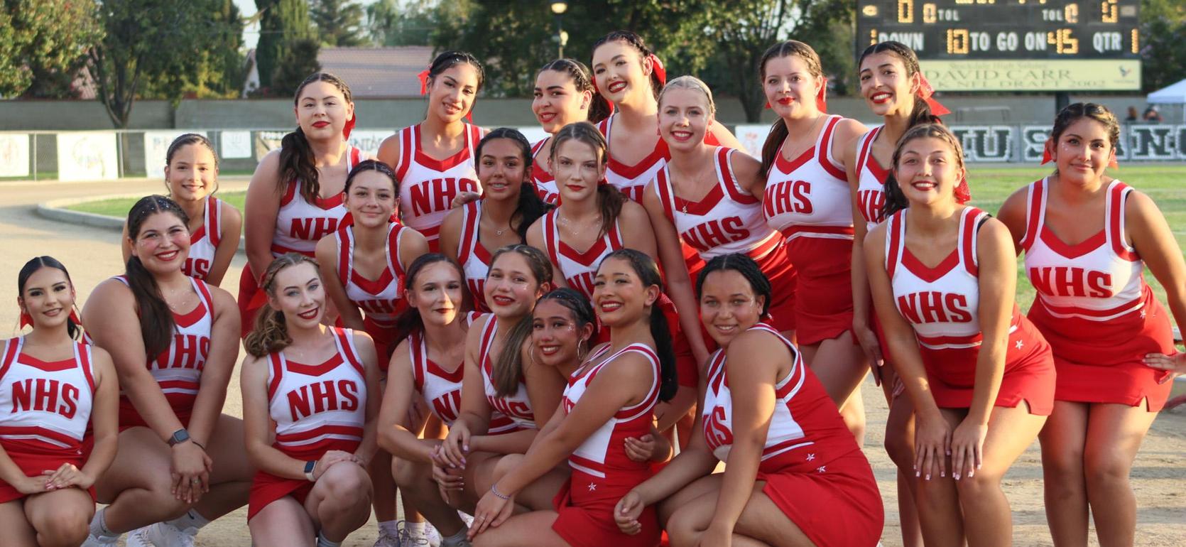A cheerleading squad in red and white uniforms poses together outdoors.