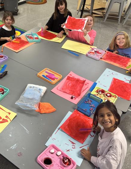 Group of children actively painting red artworks at a classroom table.